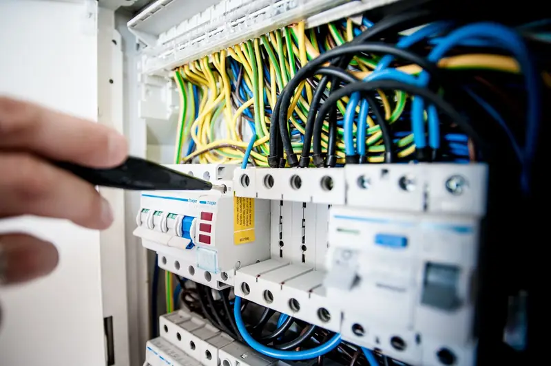 An electrician's hands testing a circuit breaker panel with a screwdriver