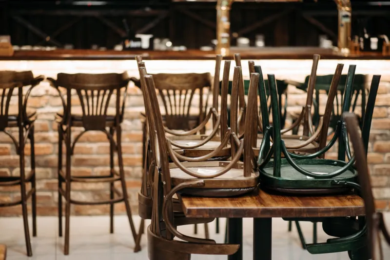 Chairs stacked upside down on tables in a closed bar room, lights low behind the counter